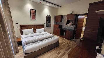 Ein Schlafzimmer mit Bett, Holz-Kopfteil, einer kleinen Küchenzeile und einer Tür zu einem weiteren Raum.