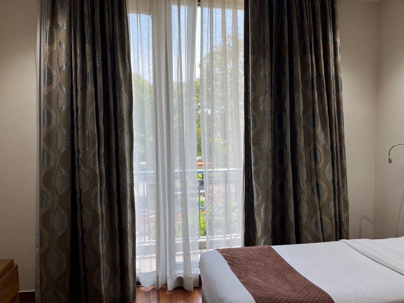 Une chambre d’hôtel avec un lit, une fenêtre avec des rideaux légers et une vue sur le balcon.