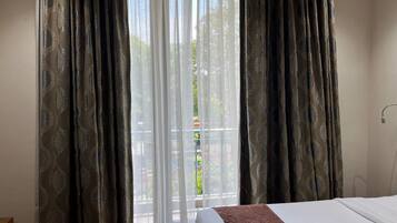Une chambre d’hôtel avec un lit, une fenêtre avec des rideaux légers et une vue sur le balcon.