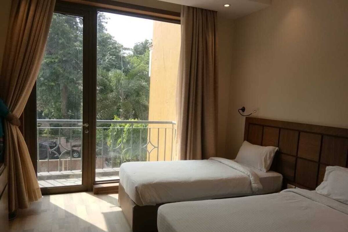 A hotel room with two beds, a balcony with a view of greenery, and a sliding glass door.