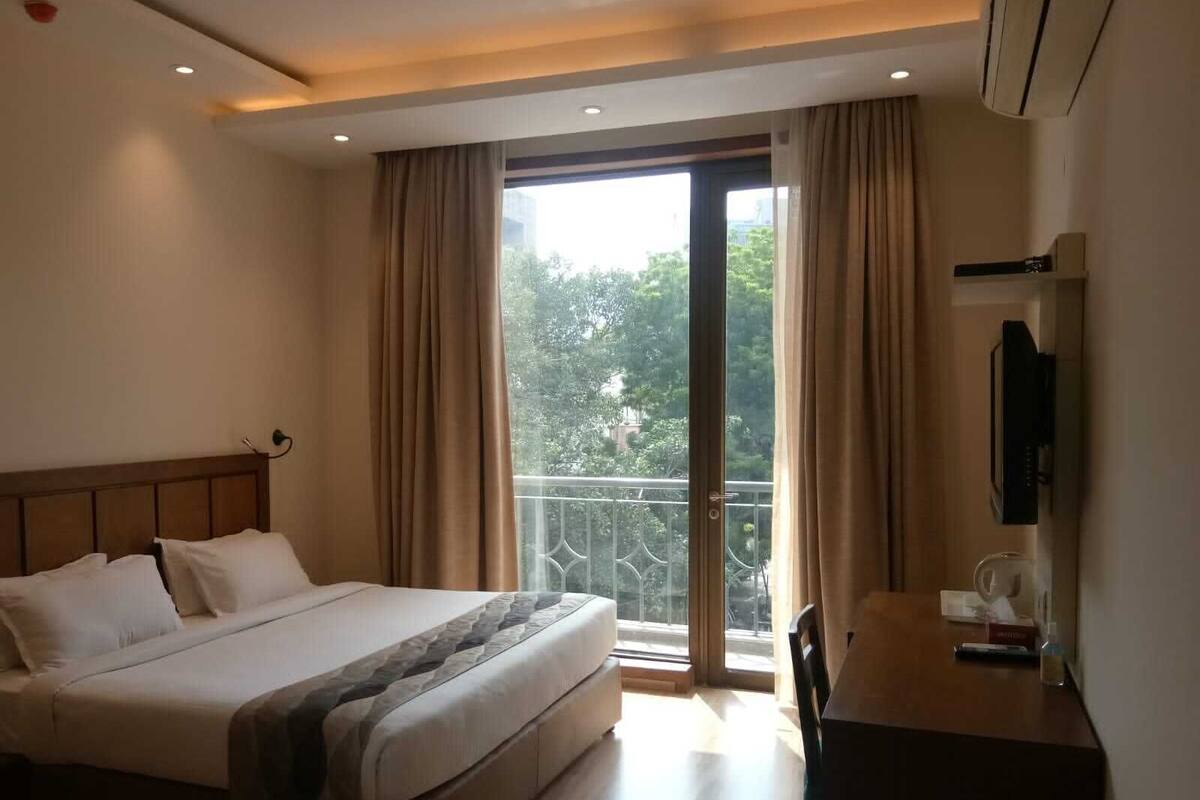 A hotel room with a bed, a desk, a TV, and a balcony with curtains.