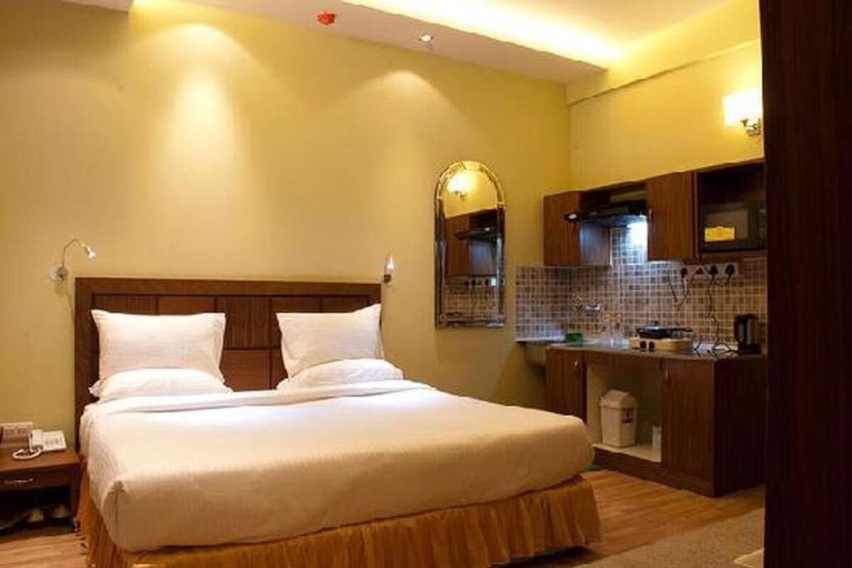A hotel room with a large bed, a small kitchenette, and a bathroom visible in the background.