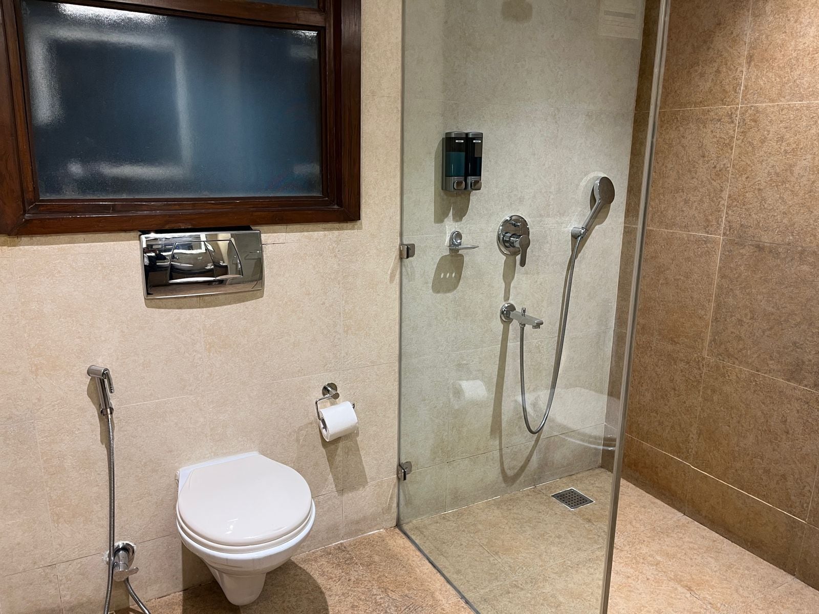 A bathroom with a glass shower enclosure, a toilet, and a hand dryer.