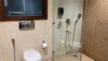 A bathroom with a glass shower enclosure, a toilet, and a hand dryer.