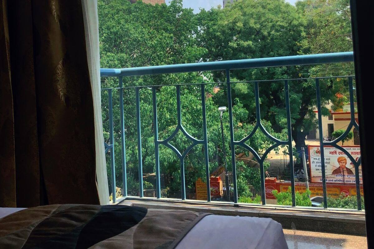 A room with a bed, a window with a view of trees and a building.