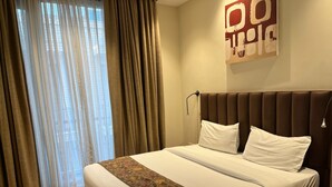 A hotel room with a large bed, a headboard, a bedside table, a lamp, and a window with curtains. - UDS Villa - Next to VFS, Walking to Connaught Place (New Delhi)