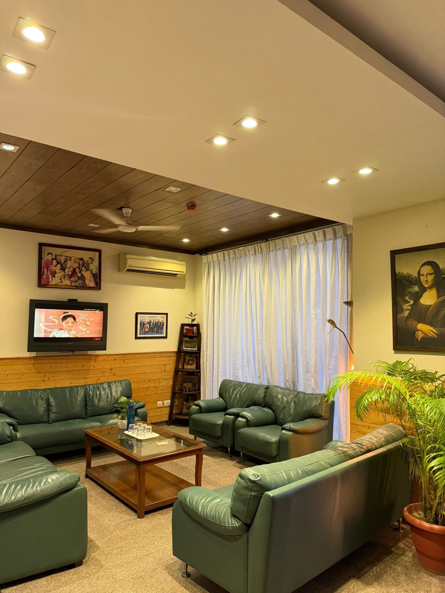 A living room with green leather sofas, a coffee table, a television, and a painting of the Mona Lisa.