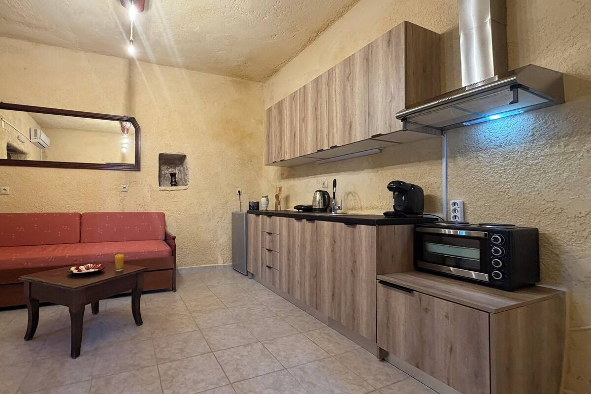 Een knus woongedeelte met een kitchenette, een bank, een bijzettafeltje en een spiegel.