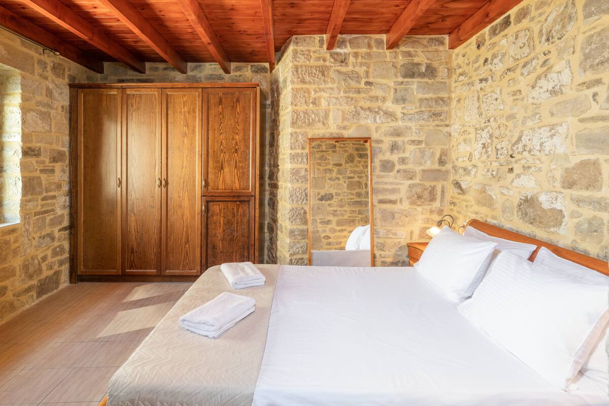 Een slaapkamer met een stenen muur, een houten garderobe en een bed met witte lakens.