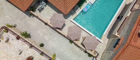 Vista aérea de un hotel con piscina, mobiliario exterior y suelo de piedra.