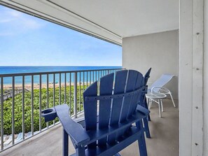A balcony with a view of the ocean, a blue Adirondack chair, and a small table with a chair. - Pelicans Paradise on the Beach (Stuart)