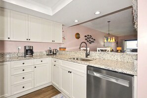 A kitchen with white cabinets, a stainless steel dishwasher, a coffee maker, and a sink. - Pelicans Paradise on the Beach (Stuart)