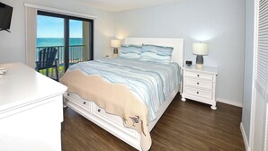 Un dormitorio con cama, mesitas de noche, cómoda y vista al océano.