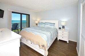 A bedroom with a bed, bedside tables, a dresser, and a view of the ocean. - Pelicans Paradise on the Beach (Stuart)