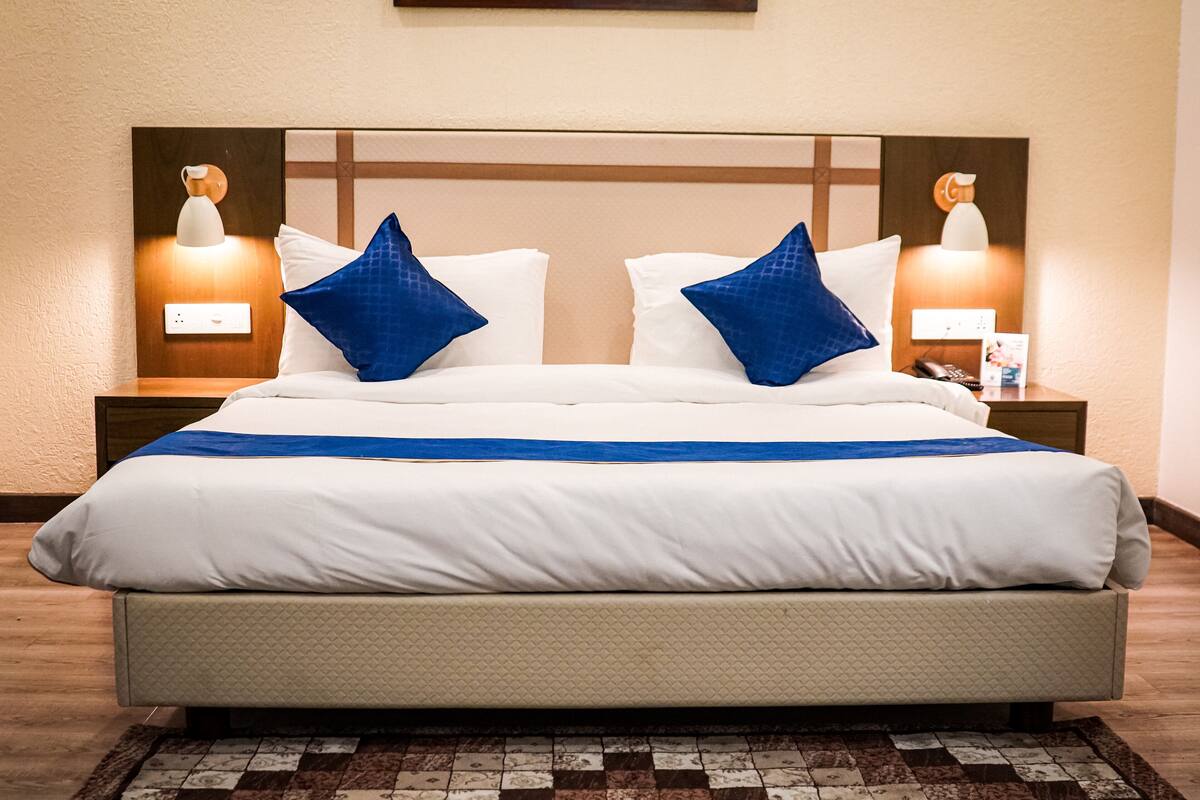 Une chambre d’hôtel avec un grand lit, deux lampes de chevet et une table de chevet sur laquelle se trouvent un téléphone et un magazine.