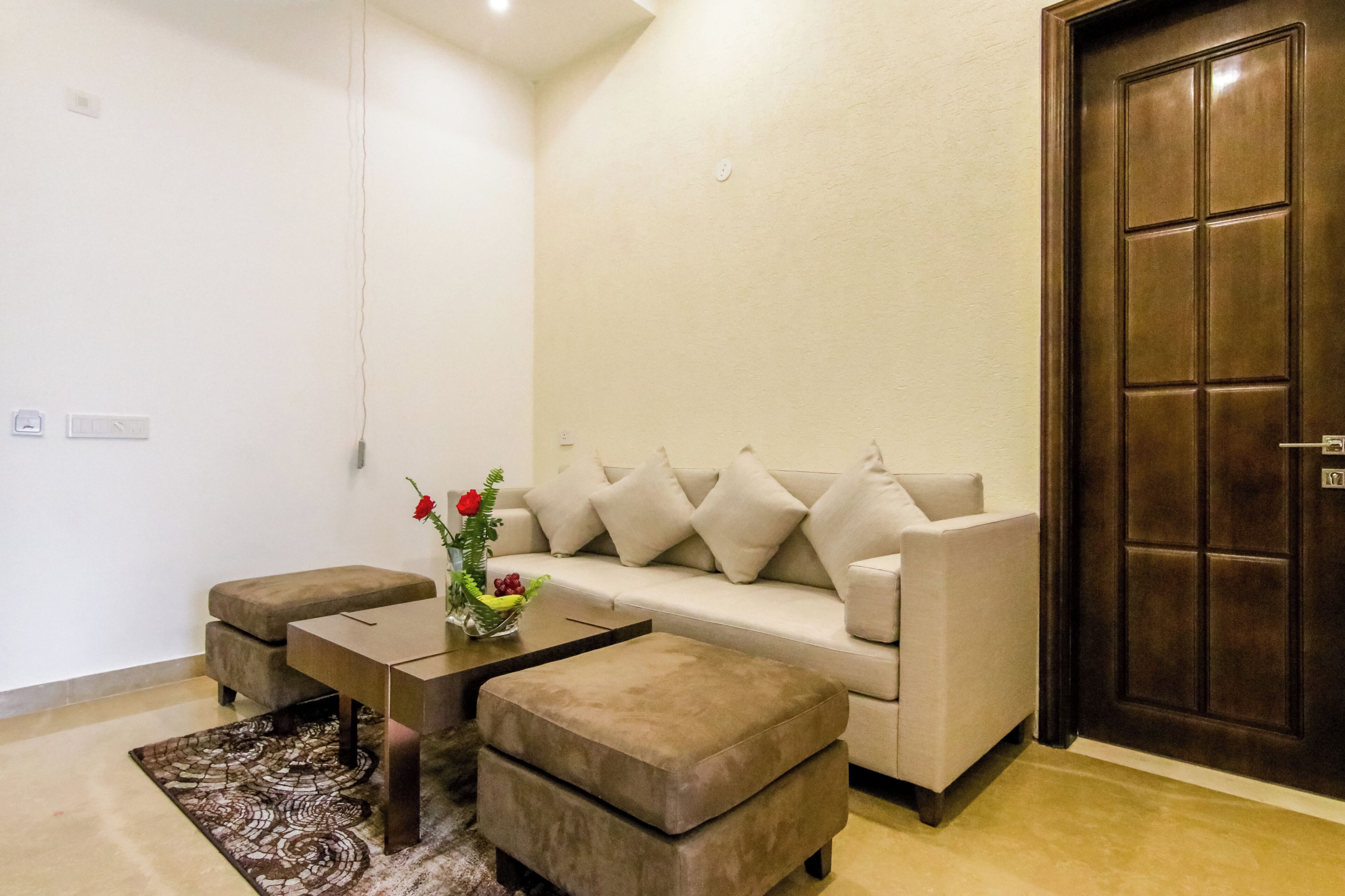 A living room with a beige sofa, two matching ottomans, a coffee table, and a vase with flowers.