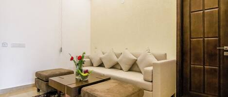 A living room with a beige sofa, two matching ottomans, a coffee table, and a vase with flowers.