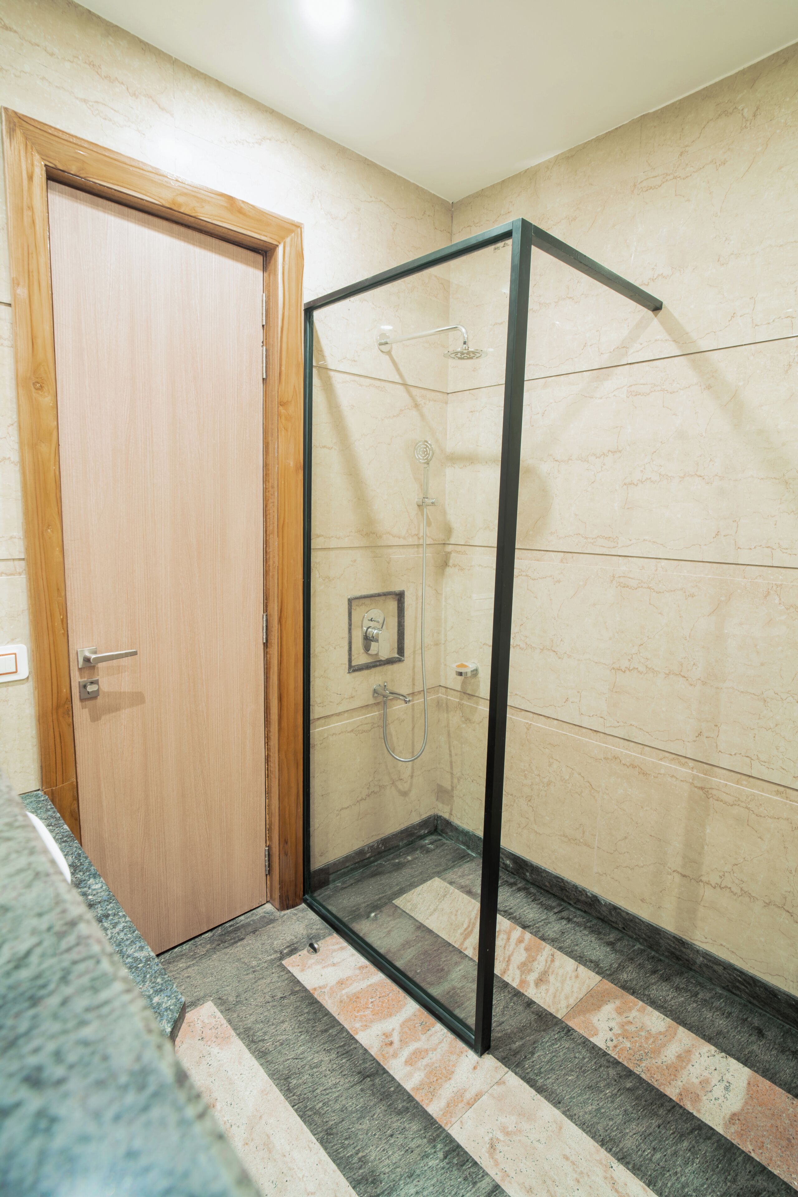 A shower enclosure with a glass door, a wooden door, and a tiled floor.