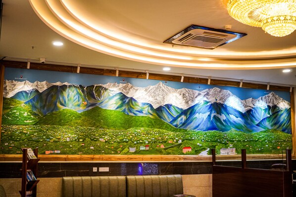Un mural que muestra montañas y un pueblo, con un mostrador de recepción y una zona de estar al frente.