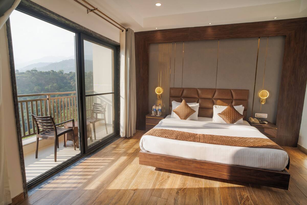 Une chambre spacieuse avec un grand lit, un balcon avec des chaises et une vue sur les montagnes.