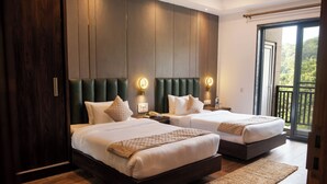 Quarto de hotel com duas camas, piso de madeira, uma janela grande com varanda e uma parede revestida em madeira escura.