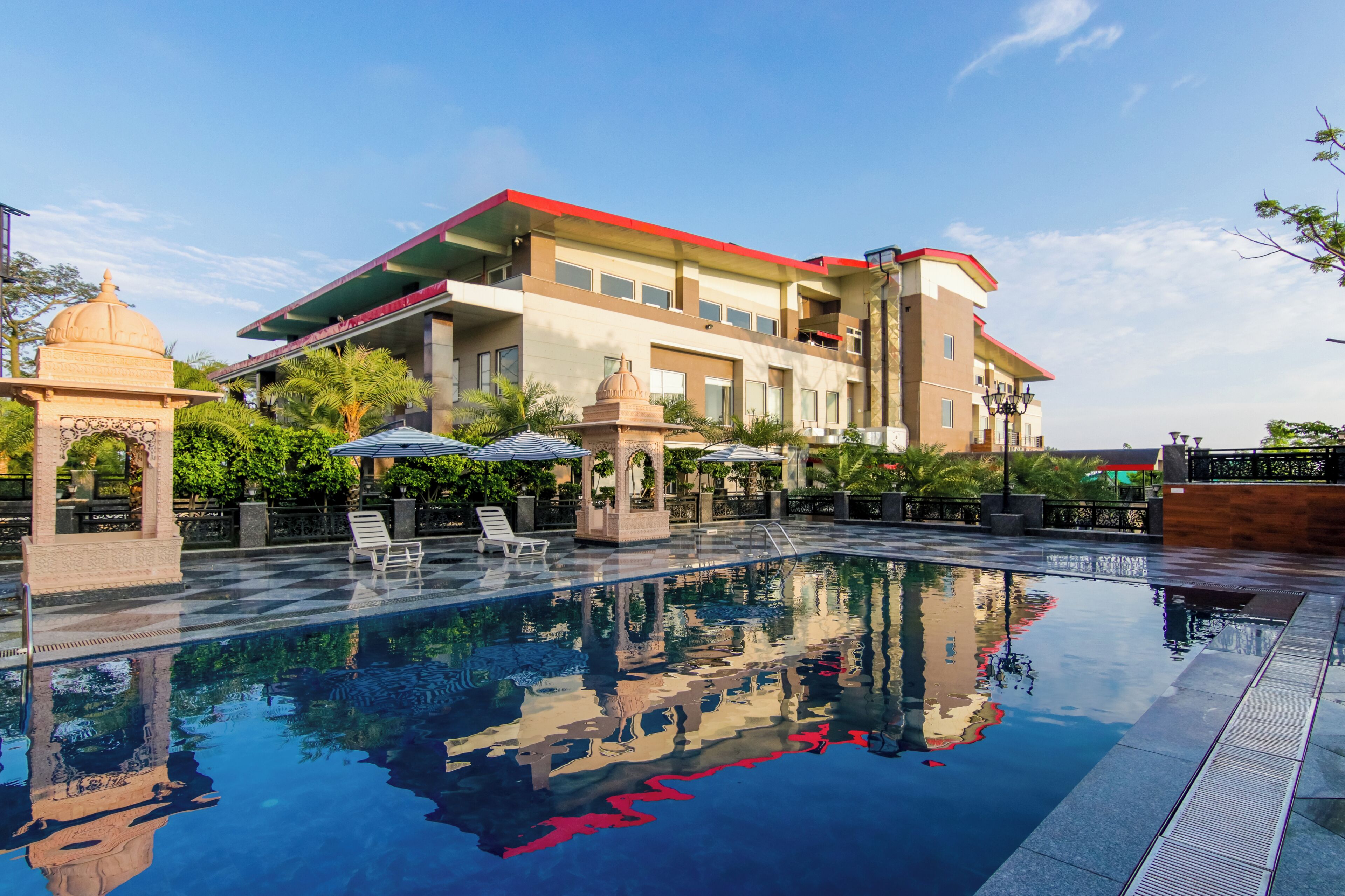 A hotel with a swimming pool, a covered area with umbrellas, and a large building with a red roof.