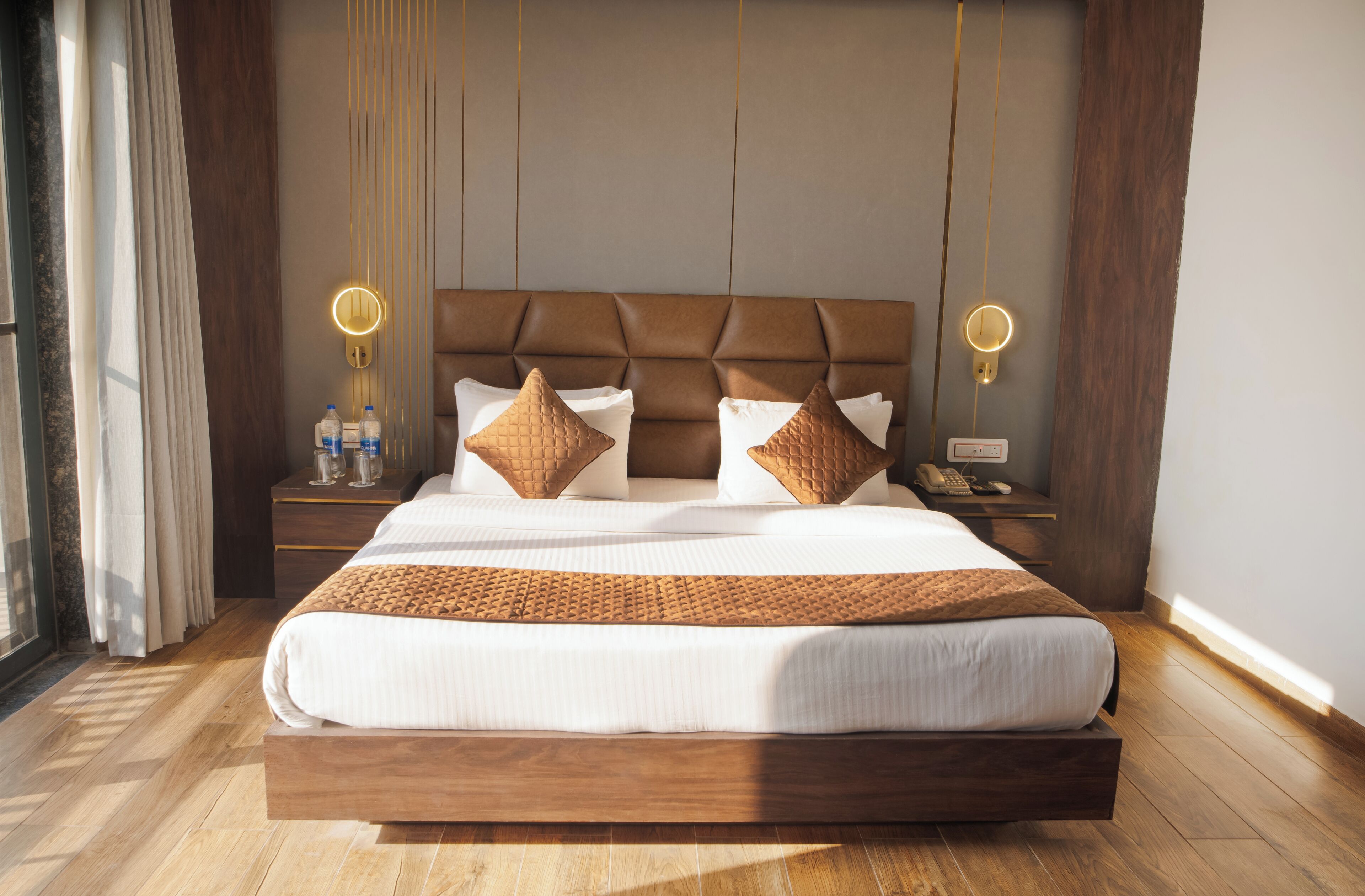 Una cama grande con estructura de madera, dos mesitas de noche con lámparas, y vista al exterior a través de una ventana.