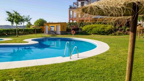 A swimming pool with a clear blue water, surrounded by a well-maintained lawn and a building with balconies in the background.