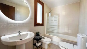 A bathroom with a large oval mirror, a sink, a toilet, and a shower.