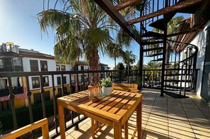 A wooden table and bench on a balcony with a view of neighboring buildings and a palm tree. - Stylish Apartment • Roof Terrace • PET01 (Ayamonte)