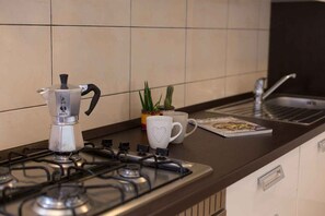 Une cuisine équipée d’une cuisinière à gaz, d’une machine à café, d’une tasse en forme de cœur, d’une plante en pot et d’un ordinateur portable posé sur le comptoir.
