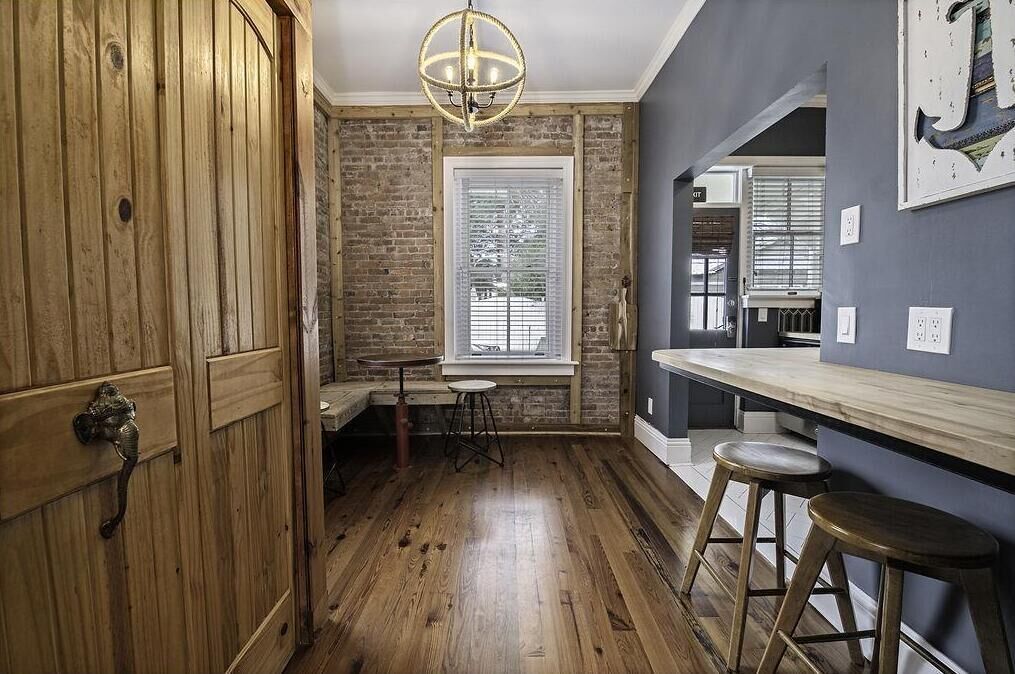 A kitchen with wooden floors, a window, a bar counter, and stools.