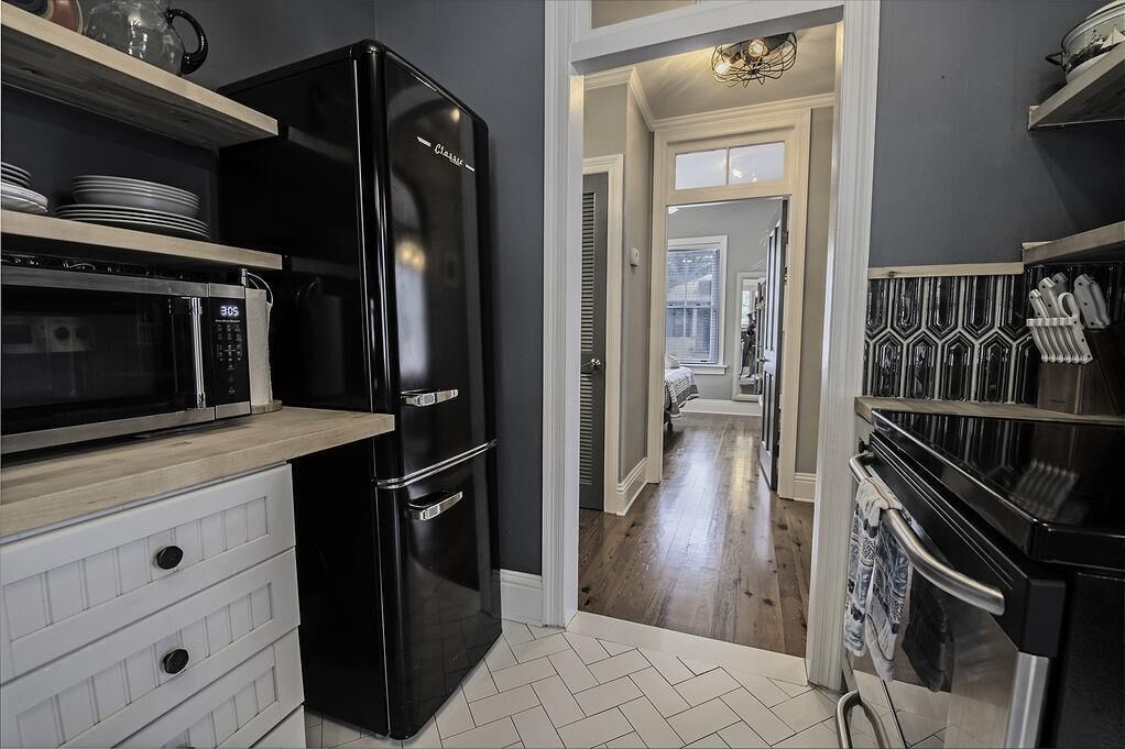 A kitchen with a black refrigerator, a microwave, and a stove. There are wooden cabinets and a tiled floor.