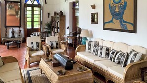 A spacious living room with wicker furniture, a large sofa with patterned cushions, and a wooden cabinet. - VILLA LOU GOA Heritage Portuguese House built 1903 Exclusive Use of Private Pool (VERLA)