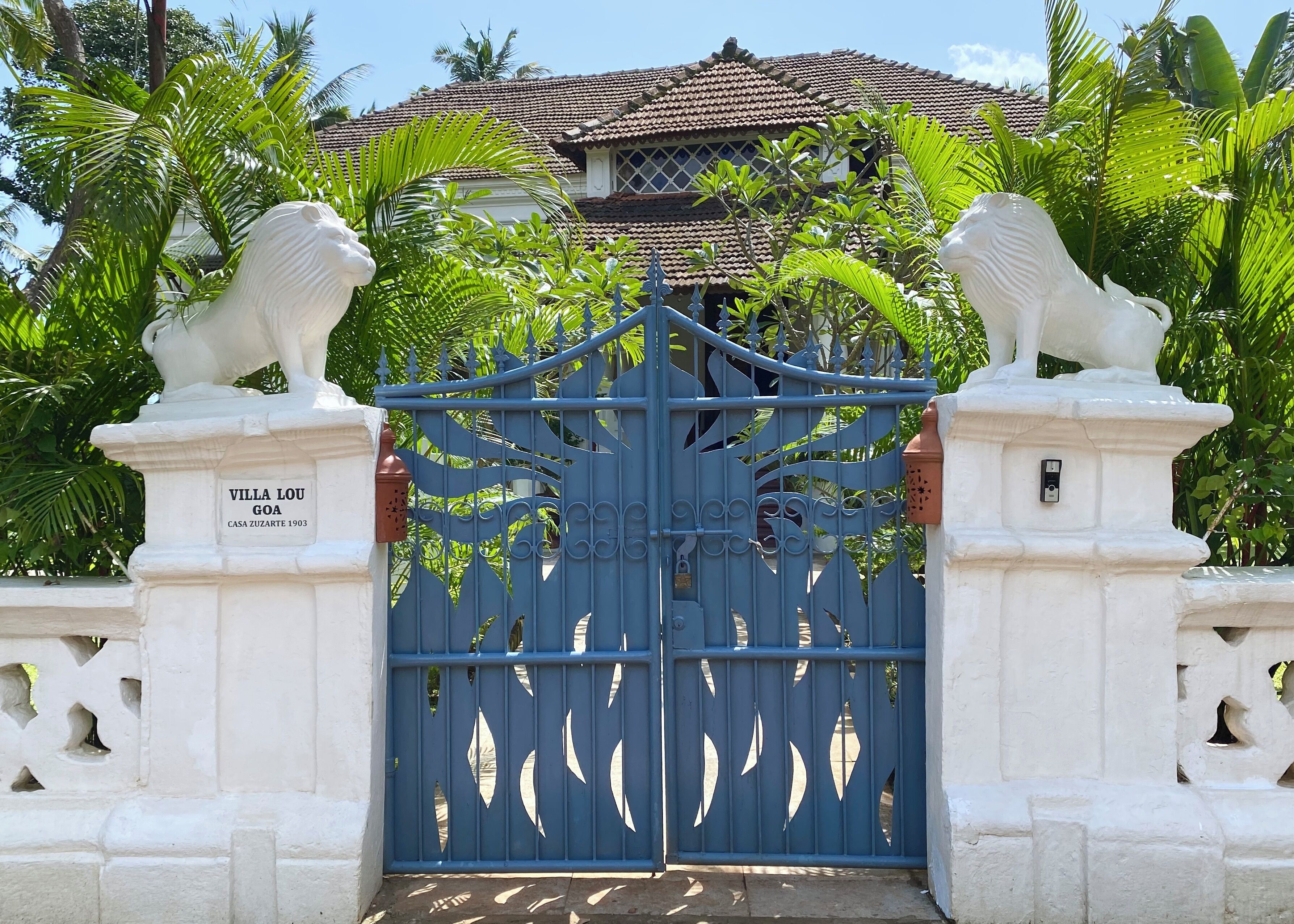 Ein verschlossenes Tor mit einem blauen Durchgang, zwei Löwenstatuen und einem Schild mit der Aufschrift 'Villa Lou Goa Casa Zuzarte 1903'.