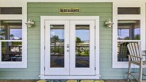 A beach house entrance with a double door, a wooden deck, and a chair outside. - Welcome to ISLAND TIME! (St. George Island)