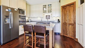 A kitchen with white cabinets, a stainless steel refrigerator, a microwave, and a wooden door. - Welcome to ISLAND TIME! (St. George Island)