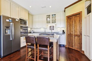 A kitchen with white cabinets, a stainless steel refrigerator, a microwave, and a wooden door.