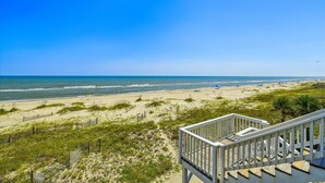 Une vue sur la plage avec un escalier en bois menant à une terrasse d’où l’on peut admirer l’océan.