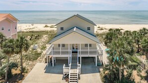 Une maison de plage à deux étages, dotée d’un balcon, d’un porche à l’avant et d’un escalier menant à l’entrée.
