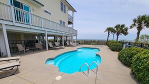 Un espace piscine avec des chaises longues et un bâtiment doté d’un balcon.