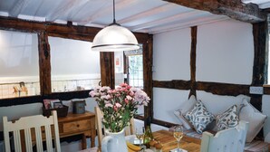A rustic dining area with a wooden table set for two, a vase of flowers, and a bottle of wine. - Corner Thatch - Worcestershire, a charming cottage sleeps 4 guests in 2 bedrooms (Abbots Morton)
