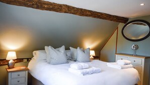 A neatly made bed with pillows and folded towels, a bedside table with a lamp, and a mirror on a dresser. - Corner Thatch - Worcestershire, a charming cottage sleeps 4 guests in 2 bedrooms (Abbots Morton)