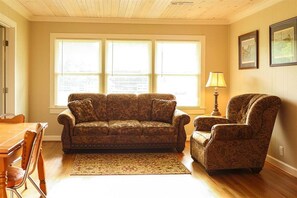 A living room with a patterned sofa, a matching armchair, a wooden dining table, and a patterned rug.
