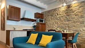 A cozy living area with a blue sofa, wooden dining table, and stone wall backdrop.