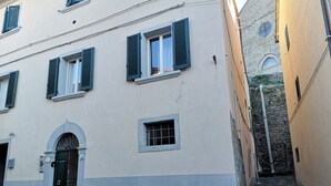 A building with a beige facade, multiple windows with shutters, and a stone staircase leading to a lower level.