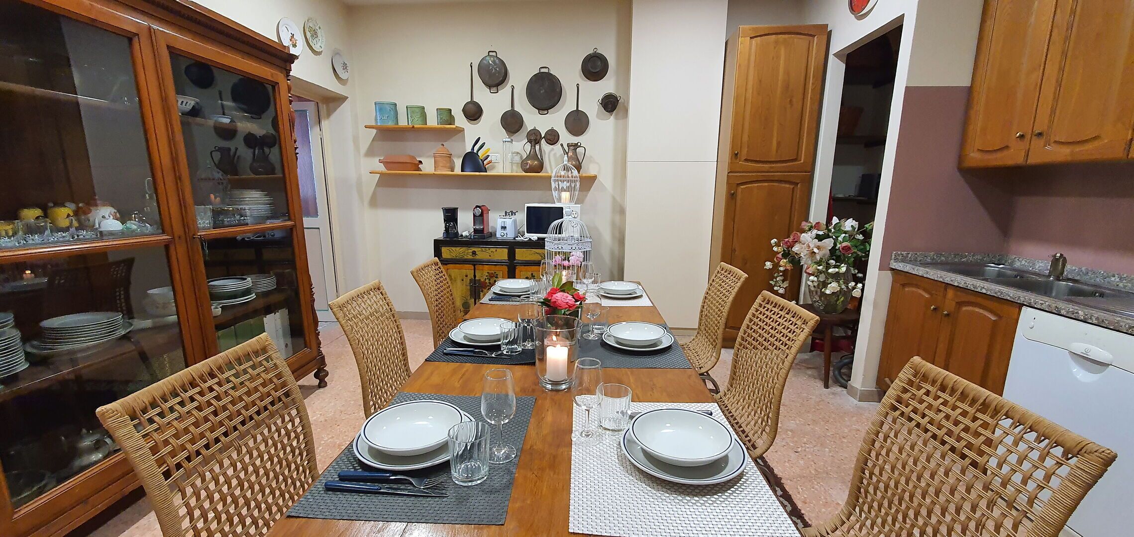 A dining room with a wooden table set for four, surrounded by wicker chairs.