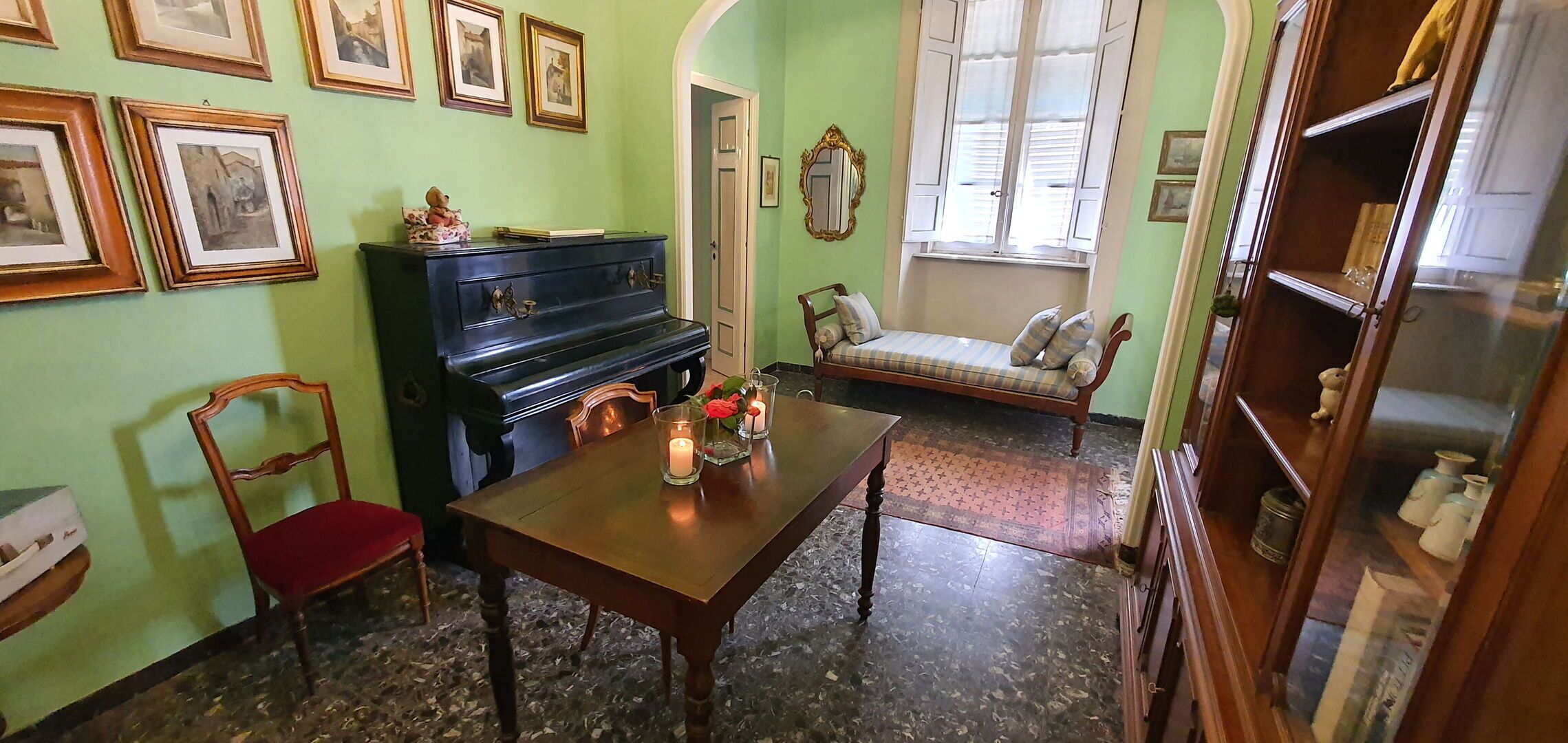 A room with a piano, a dining table with candles, a sofa, and framed pictures on the wall.