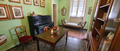 A room with a piano, a dining table with candles, a sofa, and framed pictures on the wall.