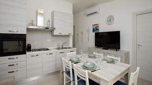 A modern kitchen with white cabinetry, a gas stove, a built-in oven, and a flat-screen TV. - Casa Perla by Wonderful Italy (Olbia)